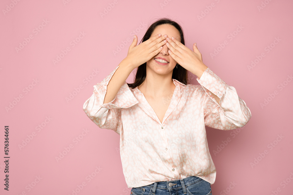 Portrait of a smiling woman in a shirt covering her eyes isolated on a pink background Portrait of a smiling woman in a shirt covering her eyes isolated on a pink background