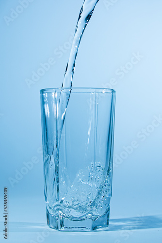 Water pours into a glass on a blue background. Clean drinking water