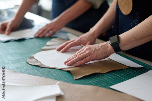 Close-up of hands of two female tailors or tanners putting sewing patterns on pieces of leather or suede while creating new attire in atelier photo