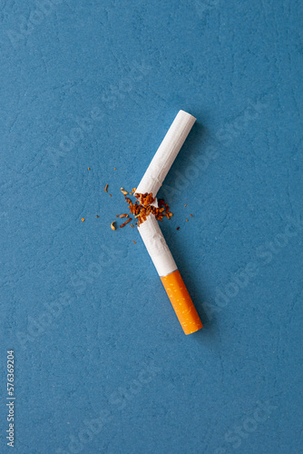 A broken cigarette with scattered tobacco for quit smoking concept. Broken cigarette on a blue background, top view