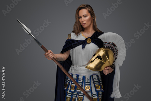 Studio shot of antique greek warrior woman dressed in blue cloak and holding golden helmet.