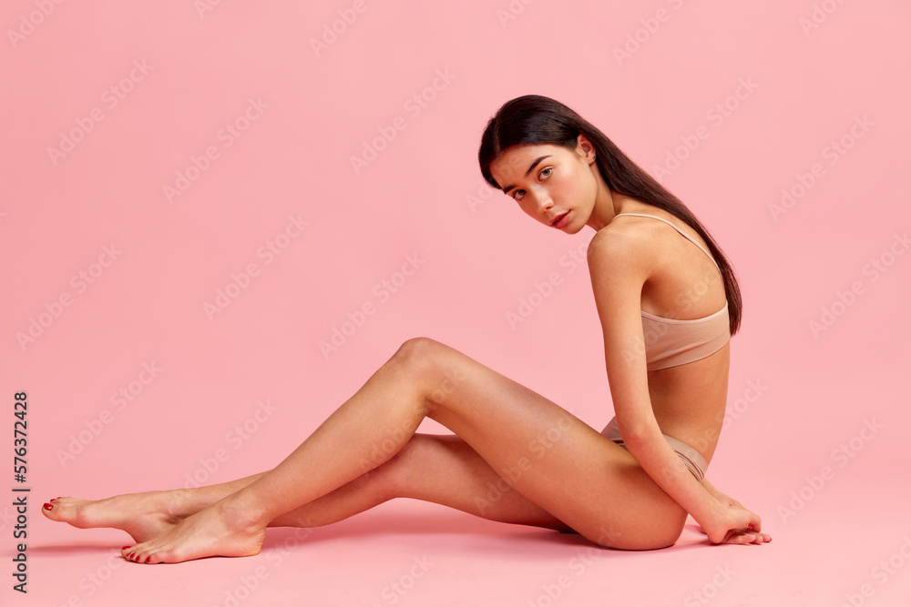 Young beautiful girl with slim figure and posing in underwear over pink studio background. Smooth legs. Depilation, epilation, laser. Concept of natural beauty, fitness, diet, body care, cosmetology Young beautiful girl with slim figure and posing in underwear over pink studio background. Smooth legs. Depilation, epilation, laser. Concept of natural beauty, fitness, diet, body care, cosmetology