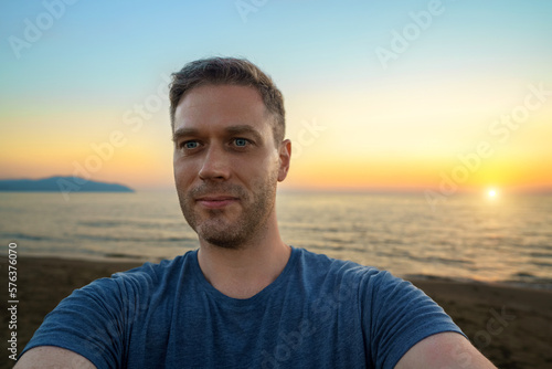 Guy taking selfie at sunset by the sea.