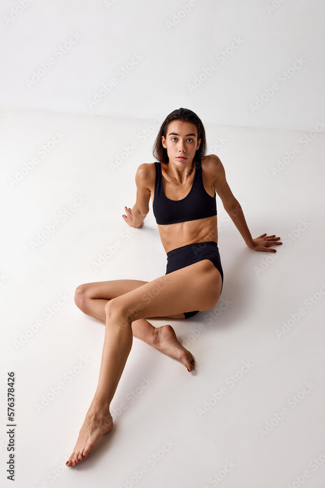 Top view of beautiful young brunette girl with slim fit body posing in black underwear over grey studio background. Concept of natural beauty, femininity, wellness, body care and fitness Top view of beautiful young brunette girl with slim fit body posing in black underwear over grey studio background. Concept of natural beauty, femininity, wellness, body care and fitness