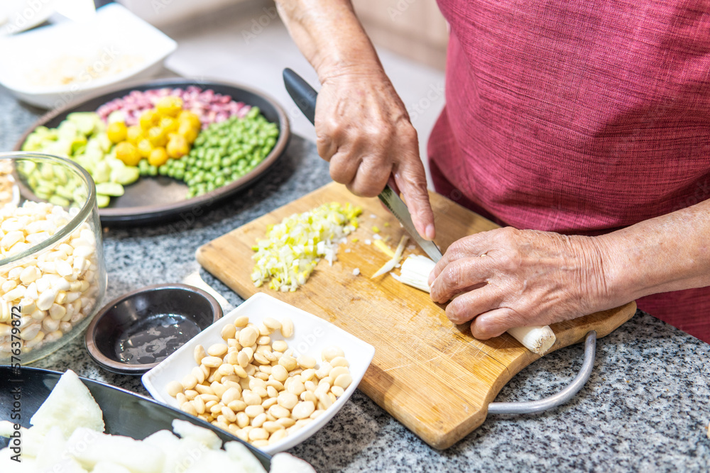 Hands of an elderly woman cutting onions with several legumes