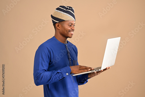 African businessman typing and smiling whiling holding his laptop isolated on a brown background photo