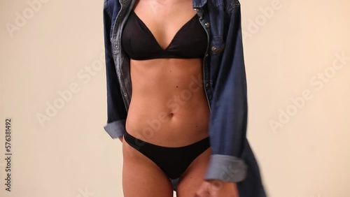 Sexy girl in an unbuttoned denim shirt and black lingerie, posing on a white background, close-up of the body. Young woman in an blue denim shirt and black sexy lingerie on a white background,close up