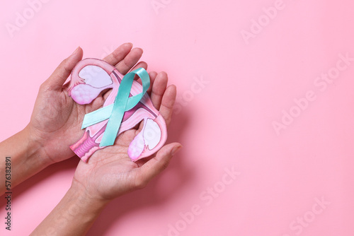Teal awareness ribbon with cervix shape on palms hand over pink background with copy space. Ovarian Cancer month, cervical cancer day.  photo