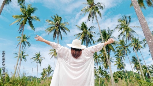 Back view of women in a straw hat standing and raising hands breathe fresh air in the coconut garden, Feeling free, Travel on holiday or summer vacation photo