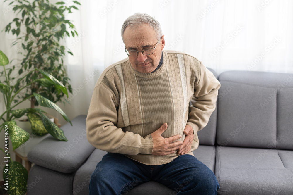 Elderly men have abdominal pain sitting on the sofa in the house. Concept Problems of the digestive tract in older people, health care.