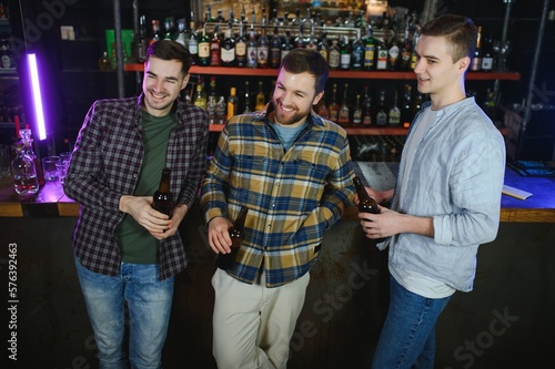 Young men in casual clothes are talking, laughing and drinking while sitting at bar counter in pub