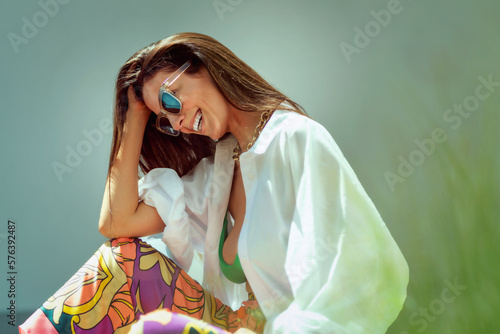 Cheerful smiling brunette woman wearing sunglasses and beachwear while relaxing outside