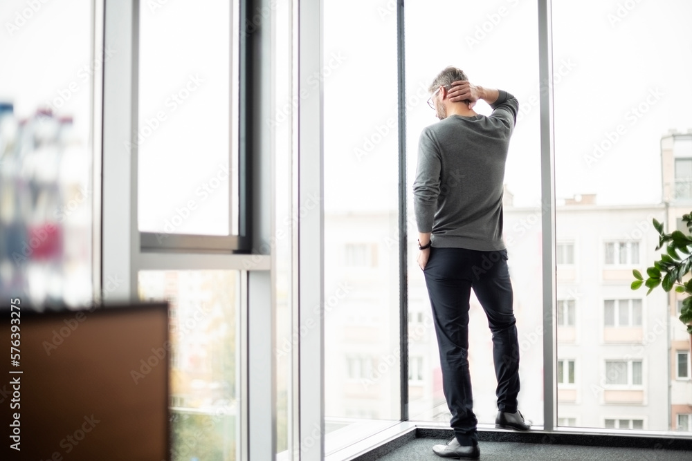 Rear view of unrecognizable businessman standing at the glass window in a modern office Rear view of unrecognizable businessman standing at the glass window in a modern office