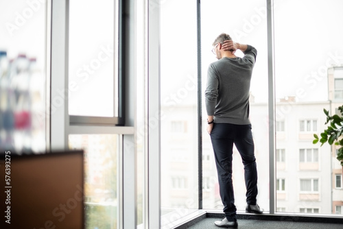 Rear view of unrecognizable businessman standing at the glass window in a modern office