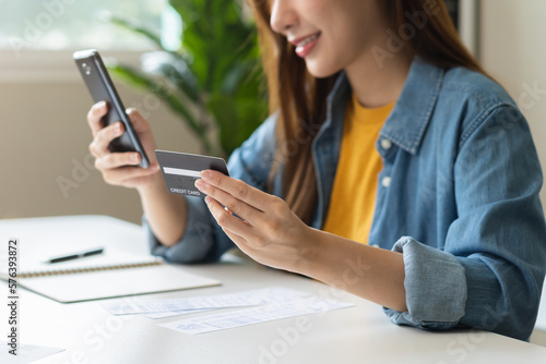 Online internet banking  smile asian young woman hand holding credit card to payment spending  using mobile phone scan qr code to transfer or pay money without cash at home. Technology of financial.
