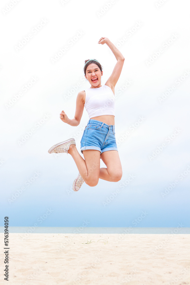 Cheerful young beautiful Asian woman having fun in white shirt and shorts jumping high on the beach. Smiling, happy to travel to the sea on weekends. travel concept Cheerful young beautiful Asian woman having fun in white shirt and shorts jumping high on the beach. Smiling, happy to travel to the sea on weekends. travel concept