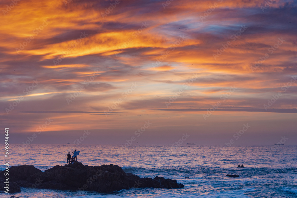 Silhouette of surfers at orange sunset on rocky beach in Porto, Portugal Silhouette of surfers at orange sunset on rocky beach in Porto, Portugal