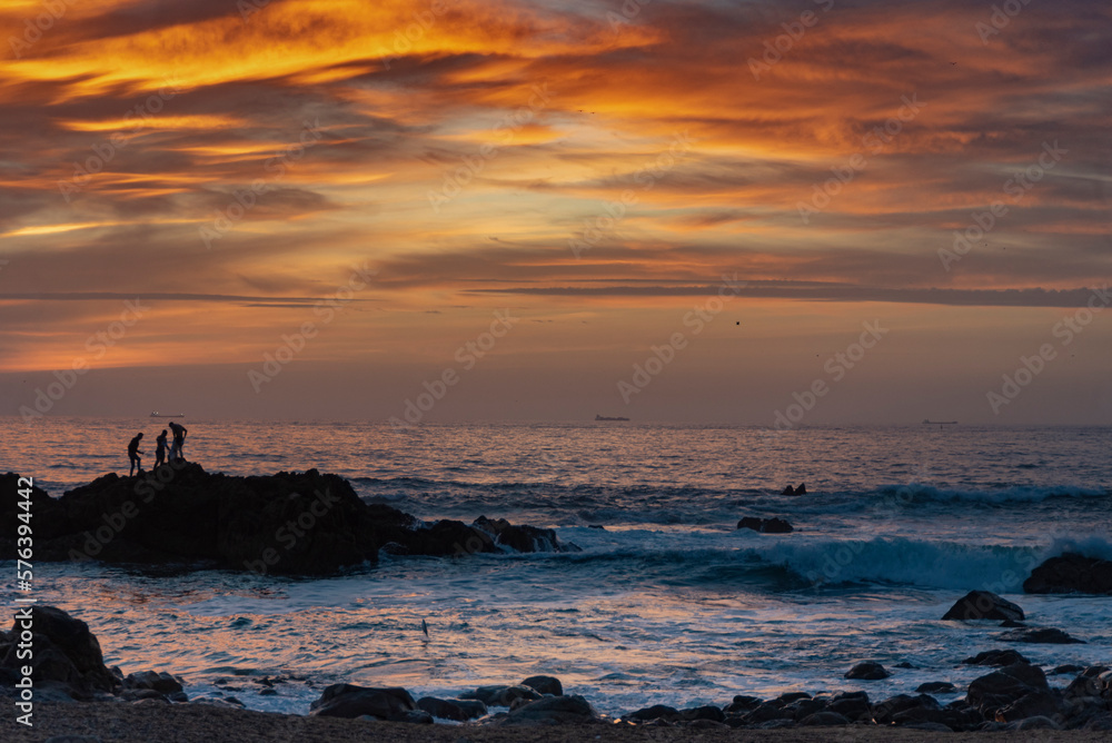 Orange sunset between rocks and clouds on beautiful beach in Porto, Portugal Orange sunset between rocks and clouds on beautiful beach in Porto, Portugal