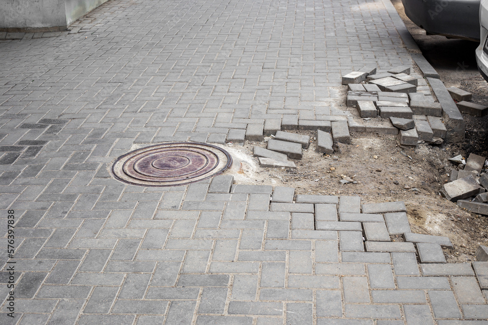 A city sidewalk with a well and crumbling paving stones. The problem of repairing bad roads