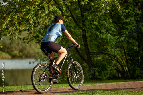 Happy brunette girl in sportswear riding a bike in the park.