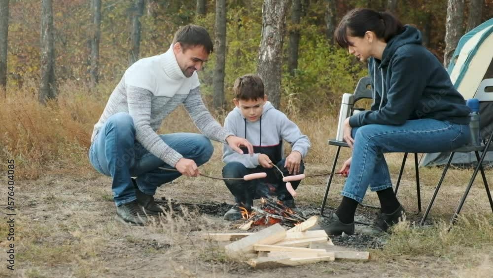 Happy Caucasian family is resting in nature in forest, bonfire has been lit and sausages are fried. Hiking in forest with your family. Camping outside on autumn. cooking food in forest. Family picnic Happy Caucasian family is resting in nature in forest, bonfire has been lit and sausages are fried. Hiking in forest with your family. Camping outside on autumn. cooking food in forest. Family picnic