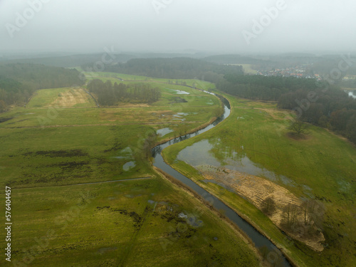 Blick auf einen kleinen geschlängelten Fluss von oben mit umgebender grüner Landschaft bei Nebel