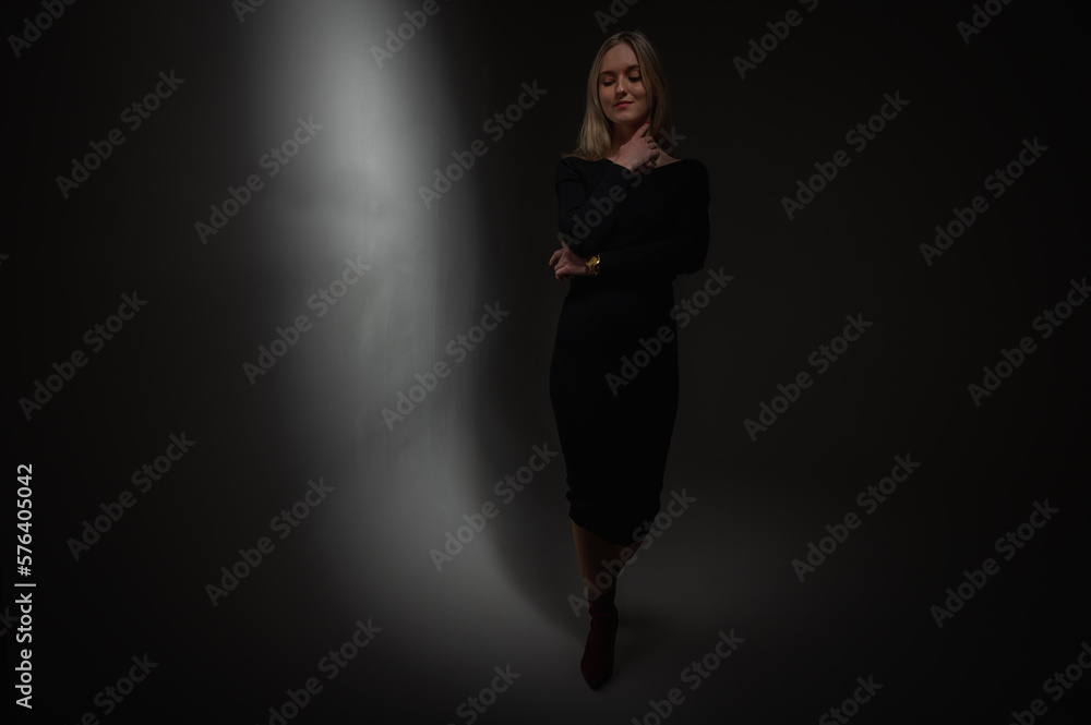 Portrait of an emotional chic girl standing in a flirtatious mood, gesturing with her hands, empty space, wearing a dark jacket on an isolated white background, place for text, beam of light, low key