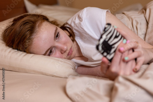Teenage girl lies in bed and looks at the phone