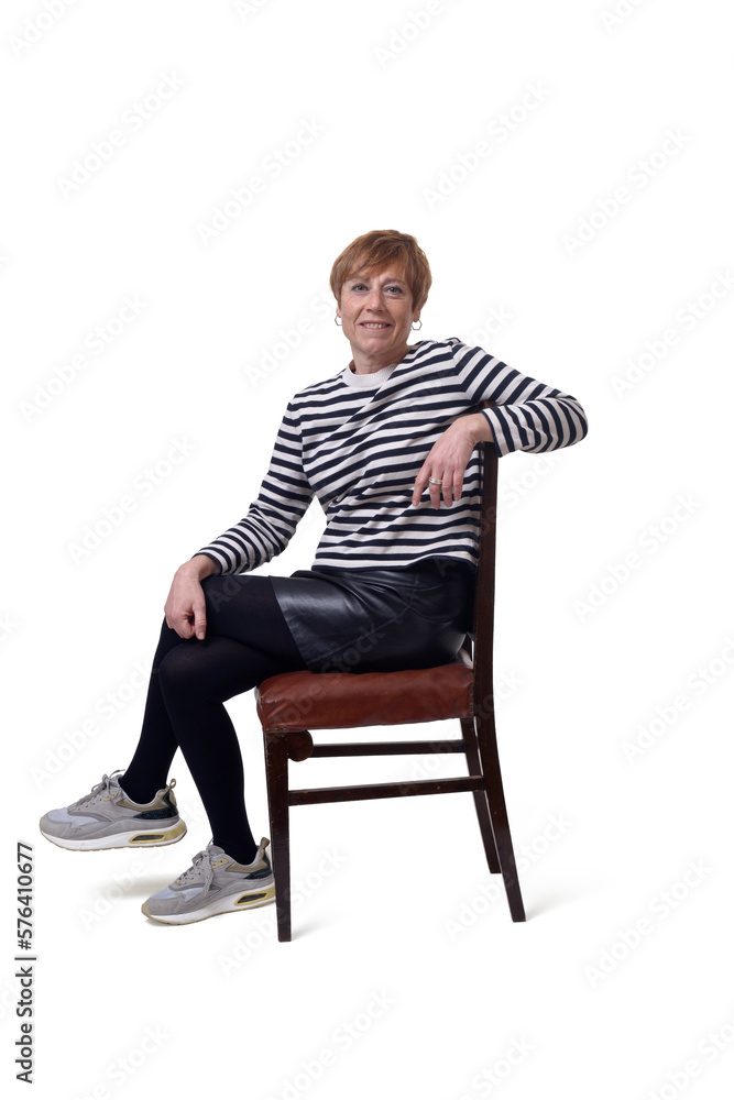 side view full length portrait of a woman in skirt, striped sweater and sneakers sitting on chair relaxed and legs crossed and looking at camera on white background side view full length portrait of a woman in skirt, striped sweater and sneakers sitting on chair relaxed and legs crossed and looking at camera on white background