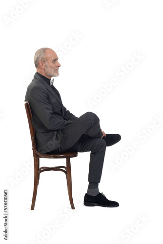 side view of a man sitting on chair with suit and bow tie legs cross legged on white background