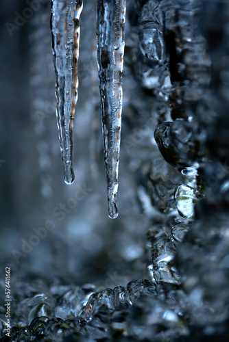 Icicles with clear water drops at a creek cascade waterfall on a very cold winters day in Sauerland Germany. Close up macro of transparent and translucent turquoise blue shapes with blurred background