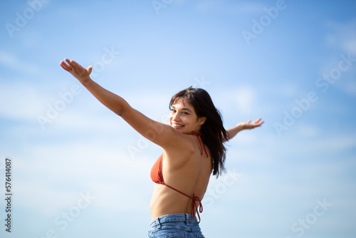 Beautiful young woman standing with hands outstretched against sky