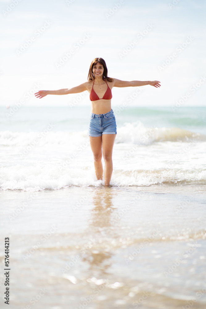 Happy young woman walking on the beach with arms outstretched