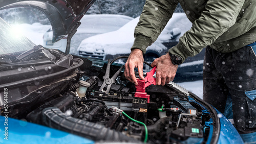 Automobile starter battery problem in winter cold weather conditions. mechanic using jumper cables to start-up a car engine. Low battery.