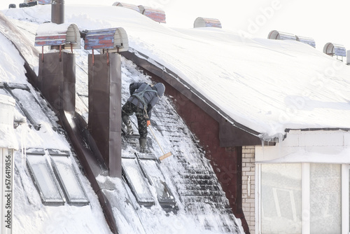 Cherepovets, Russia - February 25, 2023. The climber on the roof cleans windows from ice. Work at height. photo