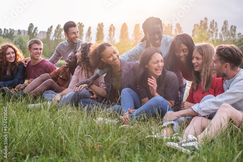 Diverse group of friends sitting on the grass at a sunset by the river. Concept: lifestyle, outdoors, diversity, multiculturalism