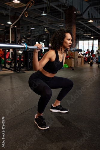Portrait of young african american woman lifting barbell while exercising in crossfit gym. Self-motivation, keep the body in good shape, athletic endurance, heavy weight training.