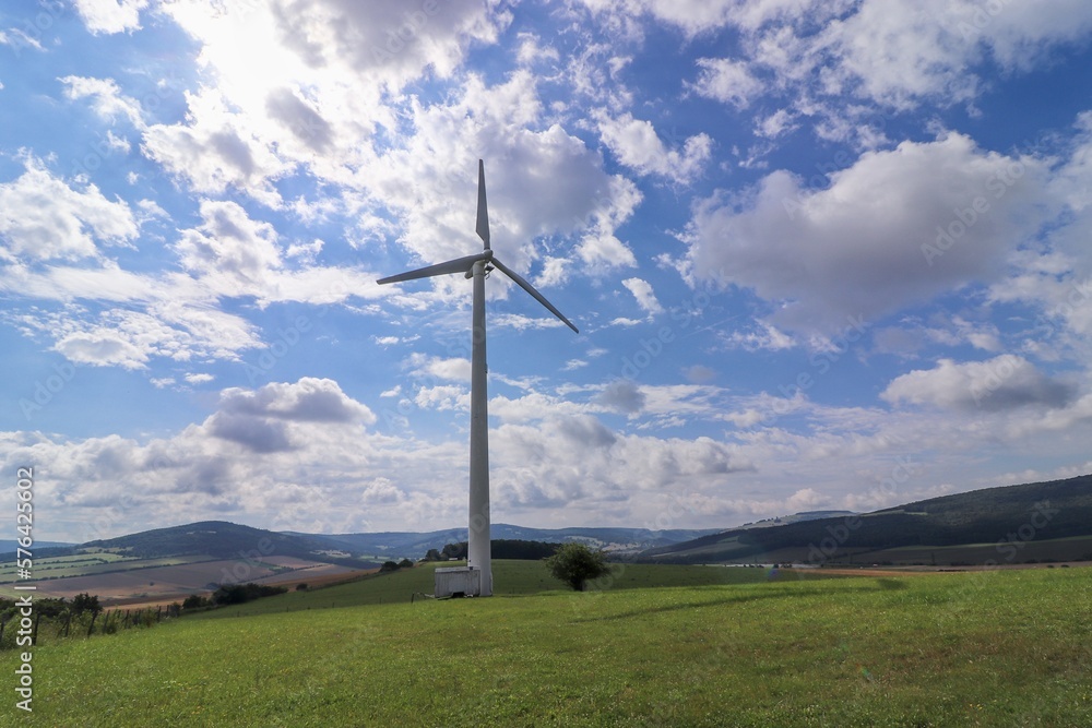 Obraz premium Wind power plant in landscape with turbine between the clouds at blue sky