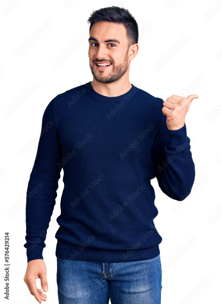 Young handsome man wearing casual clothes smiling with happy face looking and pointing to the side with thumb up. Young handsome man wearing casual clothes smiling with happy face looking and pointing to the side with thumb up.