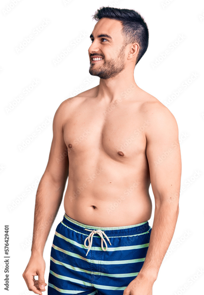 Young handsome man wearing swimwear looking away to side with smile on face, natural expression. laughing confident. Young handsome man wearing swimwear looking away to side with smile on face, natural expression. laughing confident.