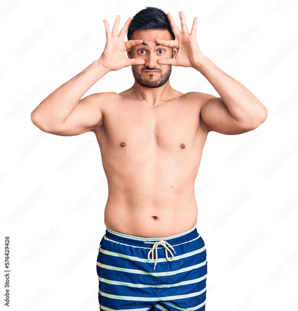 Fototapeta premium Young handsome man wearing swimwear trying to open eyes with fingers, sleepy and tired for morning fatigue