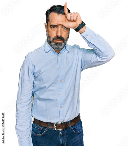 Middle aged man with beard wearing business shirt making fun of people with fingers on forehead doing loser gesture mocking and insulting.