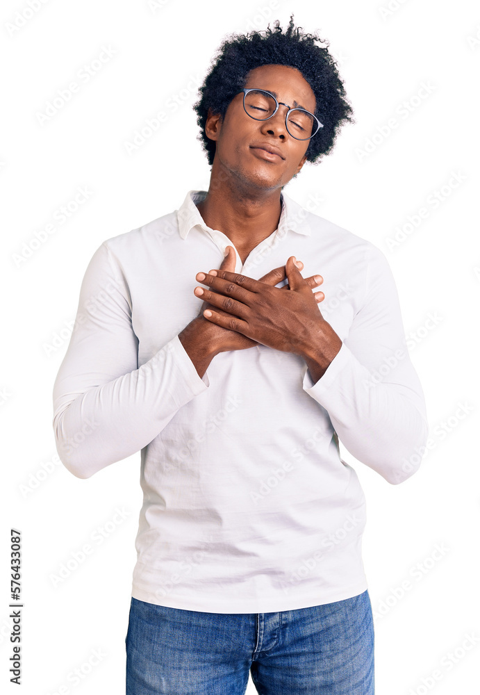 Handsome african american man with afro hair wearing casual clothes and glasses smiling with hands on chest with closed eyes and grateful gesture on face. health concept. Handsome african american man with afro hair wearing casual clothes and glasses smiling with hands on chest with closed eyes and grateful gesture on face. health concept.
