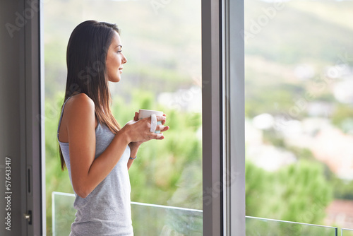What a way to start the day. Shot of an attractive young female looking at her view while having coffee.