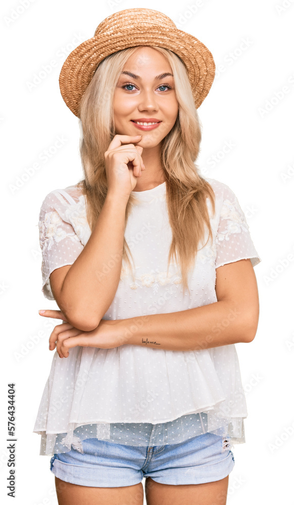 Young blonde girl wearing summer hat looking confident at the camera with smile with crossed arms and hand raised on chin. thinking positive. Young blonde girl wearing summer hat looking confident at the camera with smile with crossed arms and hand raised on chin. thinking positive.