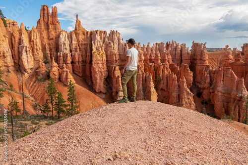 Man with scenic aerial view of hoodoo sandstone rock formations on Queens Garden trail in Bryce Canyon National Park, Utah, USA. Pine tree forest surrounded by natural amphitheatre on sunny summer day
