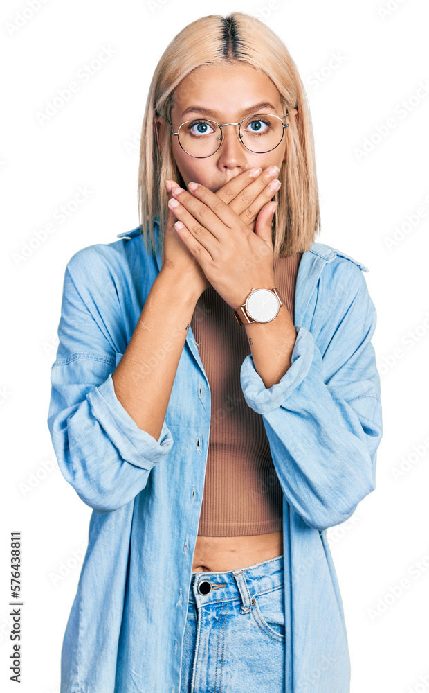 Beautiful young blonde woman wearing glasses shocked covering mouth with hands for mistake. secret concept. Beautiful young blonde woman wearing glasses shocked covering mouth with hands for mistake. secret concept.