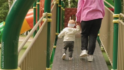 Mom holds her young child's hand and helps her take first steps on the playground