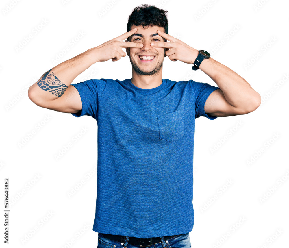 Young hispanic man wearing casual t shirt doing peace symbol with fingers over face, smiling cheerful showing victory Young hispanic man wearing casual t shirt doing peace symbol with fingers over face, smiling cheerful showing victory