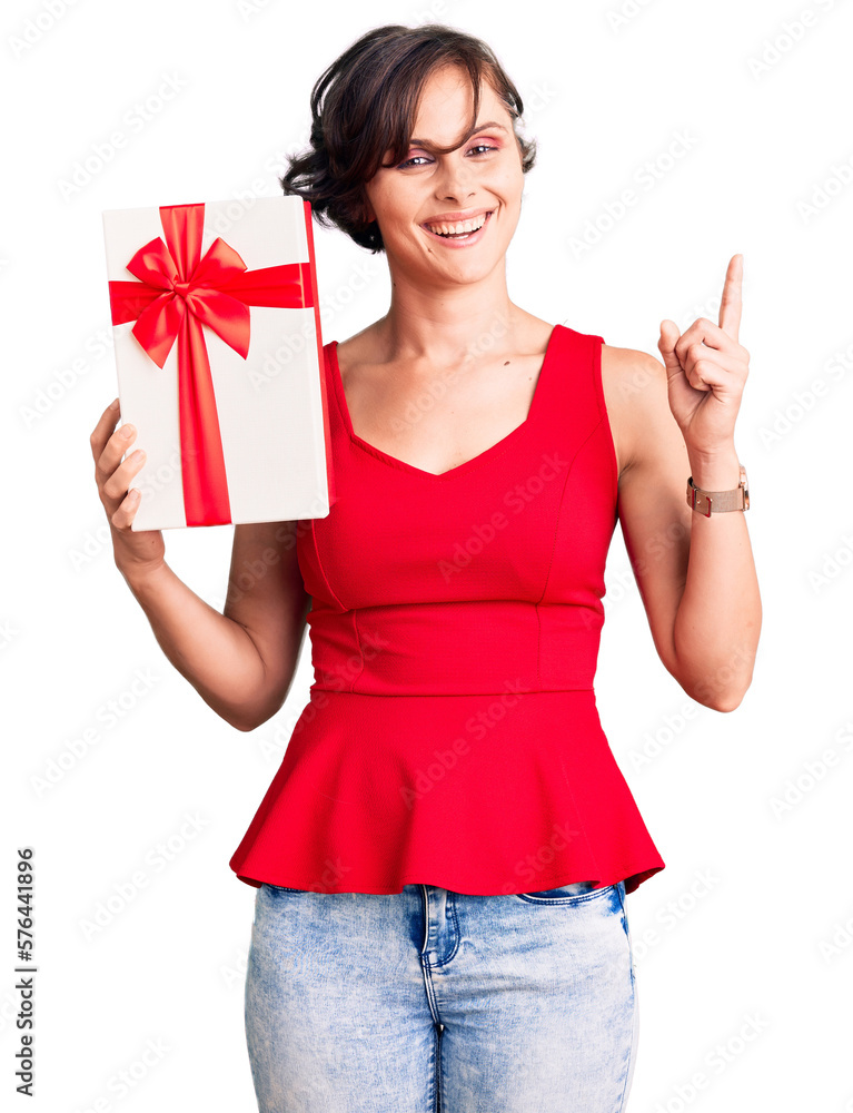 Beautiful young woman with short hair holding gift surprised with an idea or question pointing finger with happy face, number one Beautiful young woman with short hair holding gift surprised with an idea or question pointing finger with happy face, number one